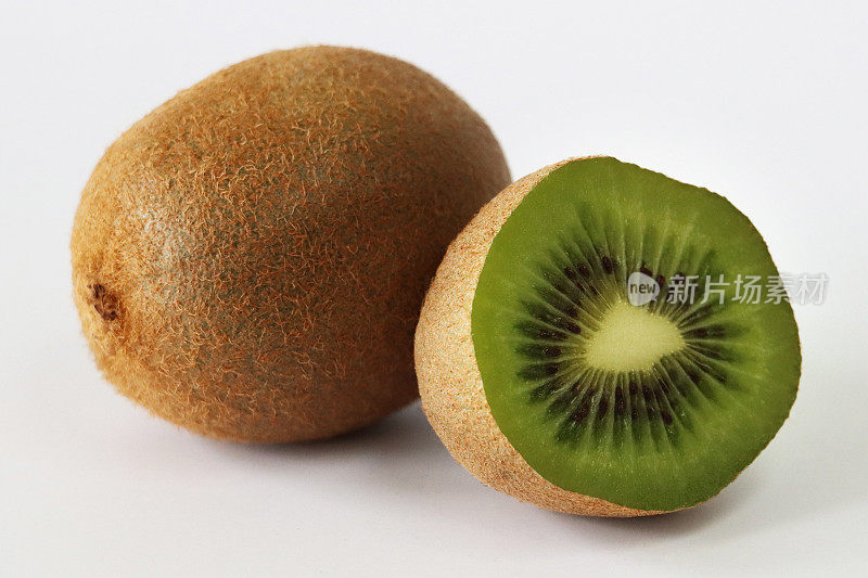 整个猕猴桃(Actinidia chinensis)的特写图像，一半的中国醋栗显示模糊的棕色皮肤和亮绿色的果肉，黑色的种子环，白色背景，重点在前景
